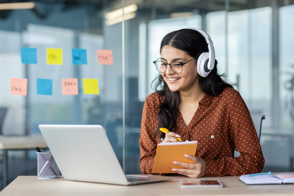 Woman wearing headphones at a computer taking notes